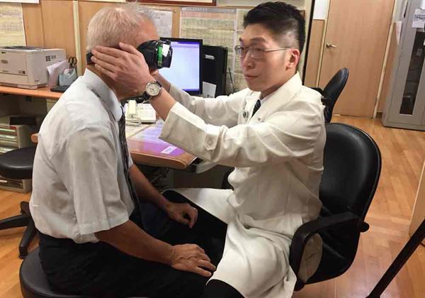 黃韻誠醫師(右)利用頭位眼震檢查儀器，找出李爺爺(左)病灶原因。(圖片提供／台北慈濟醫院)